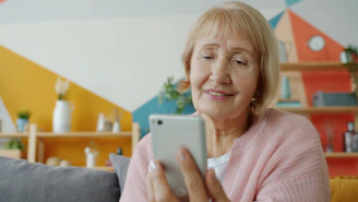 Elderly woman smiling while looking at smartphone.