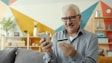 Elderly man uses smartphone and credit card for online shopping.