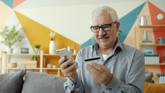 Elderly man uses smartphone and credit card for online shopping.