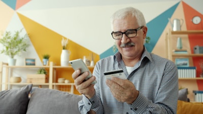 Elderly man uses smartphone and credit card for online shopping.