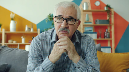 Elderly man with glasses resting chin on hands.