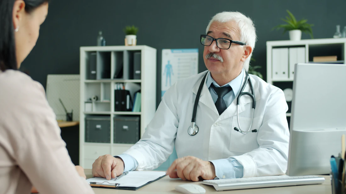 A physician shaking hands with a patient across a desk in a modern practice office