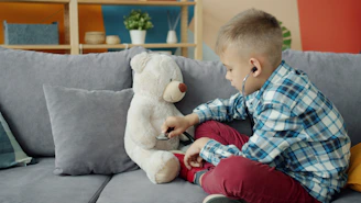 Boy listens to teddy bear with stethoscope on couch