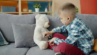 Boy listens to teddy bear with stethoscope on couch