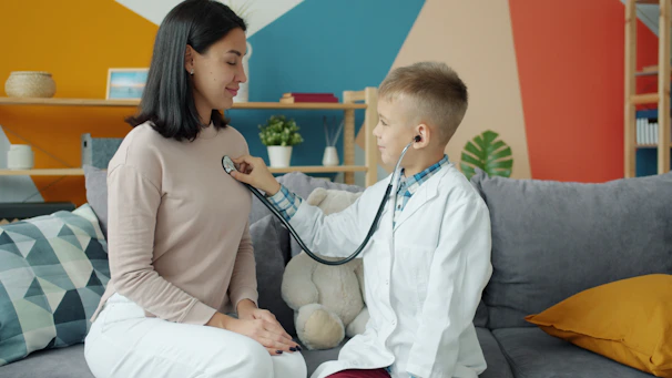 Boy in doctor's coat listens to mother's chest