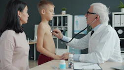 Doctor examines boy's chest with stethoscope while mother watches.
