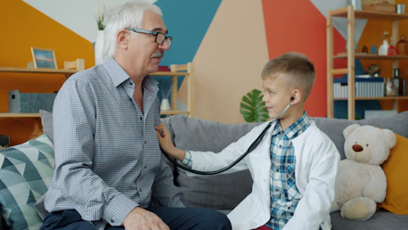 Boy in doctor's coat listens to grandfather's chest