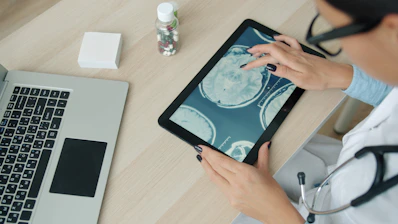 Doctor examining brain scan on tablet at desk.
