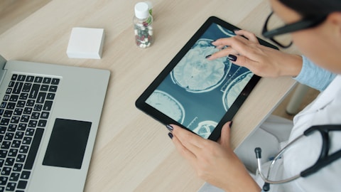Doctor examining brain scan on tablet at desk.