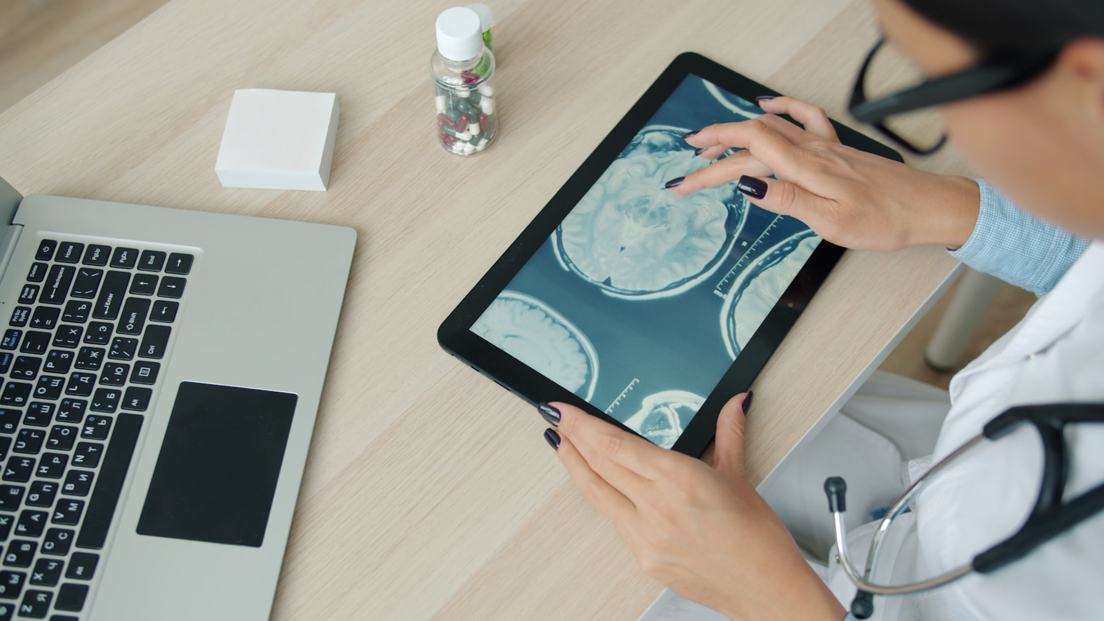 Doctor examining brain scan on tablet at desk, representing the convergence of medical expertise and digital health technology in the AI era.