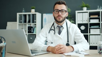 Doctor wearing a white coat sits at a desk.