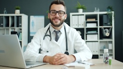 Doctor wearing a stethoscope sits at a desk.