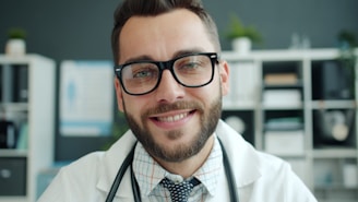 Smiling doctor wearing glasses and stethoscope in office.