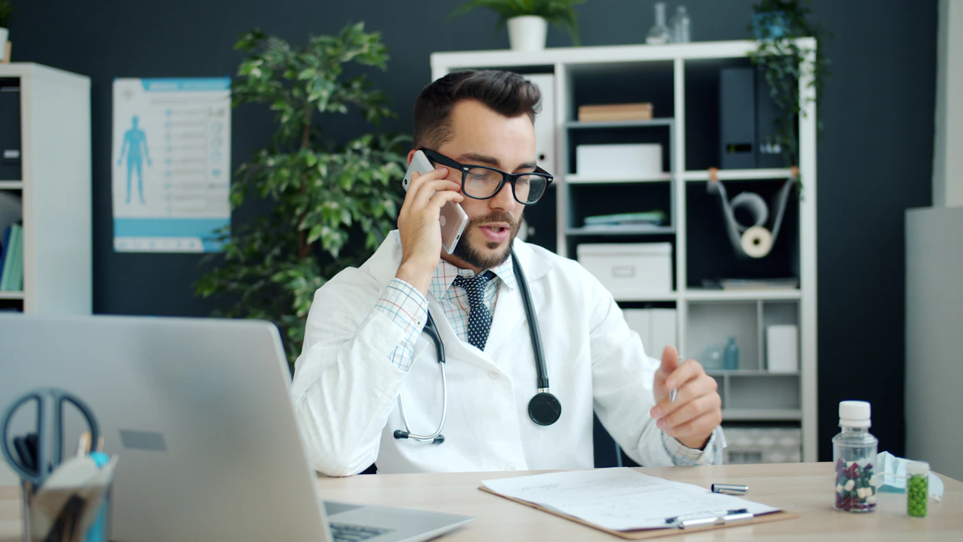 A Licensed Clinical Doctor in a white coat at a tidy office desk with a patient clipboard and laptop