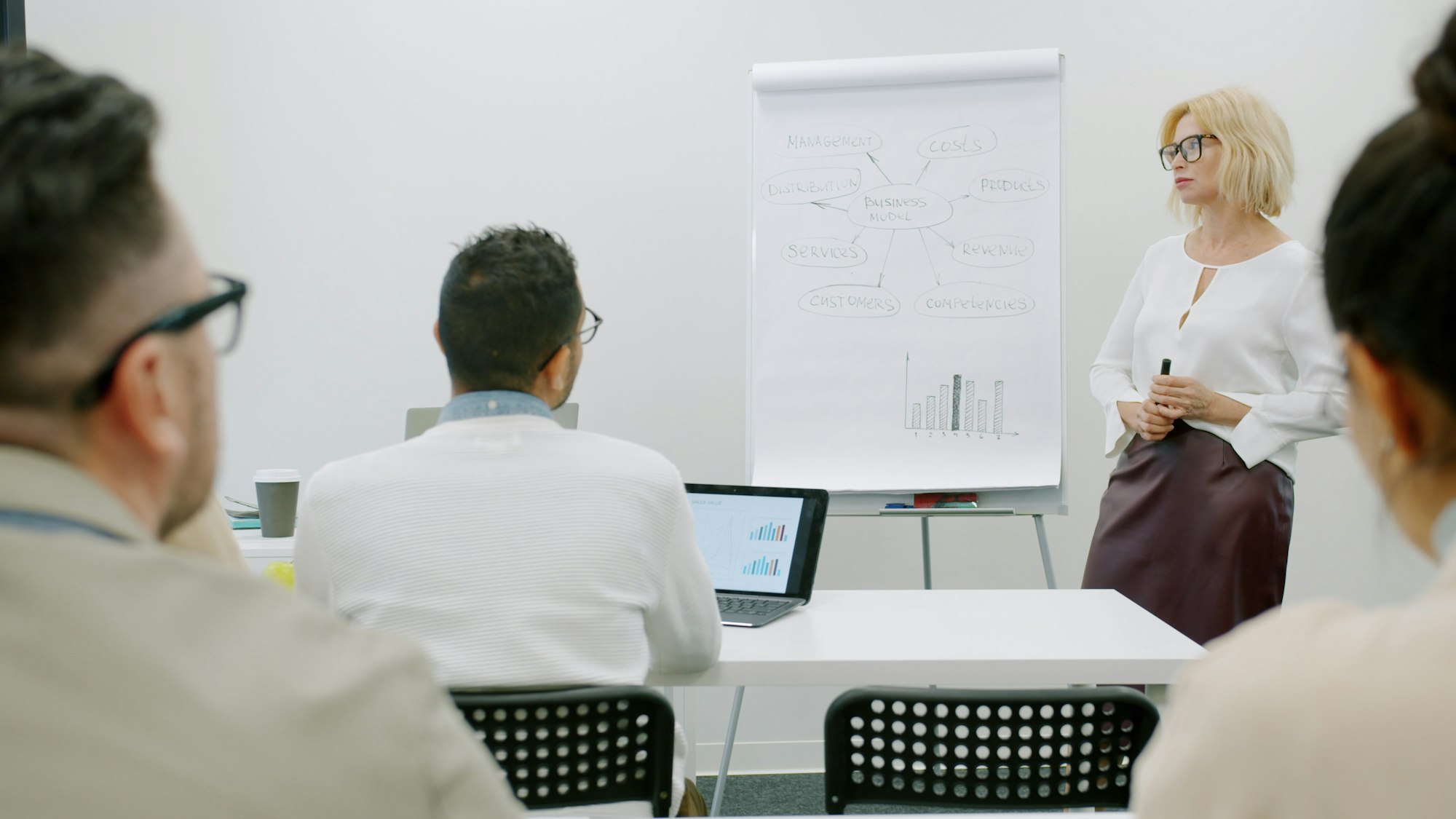 Woman facilitator presenting to a group of attendees in a modern corporate workshop setting