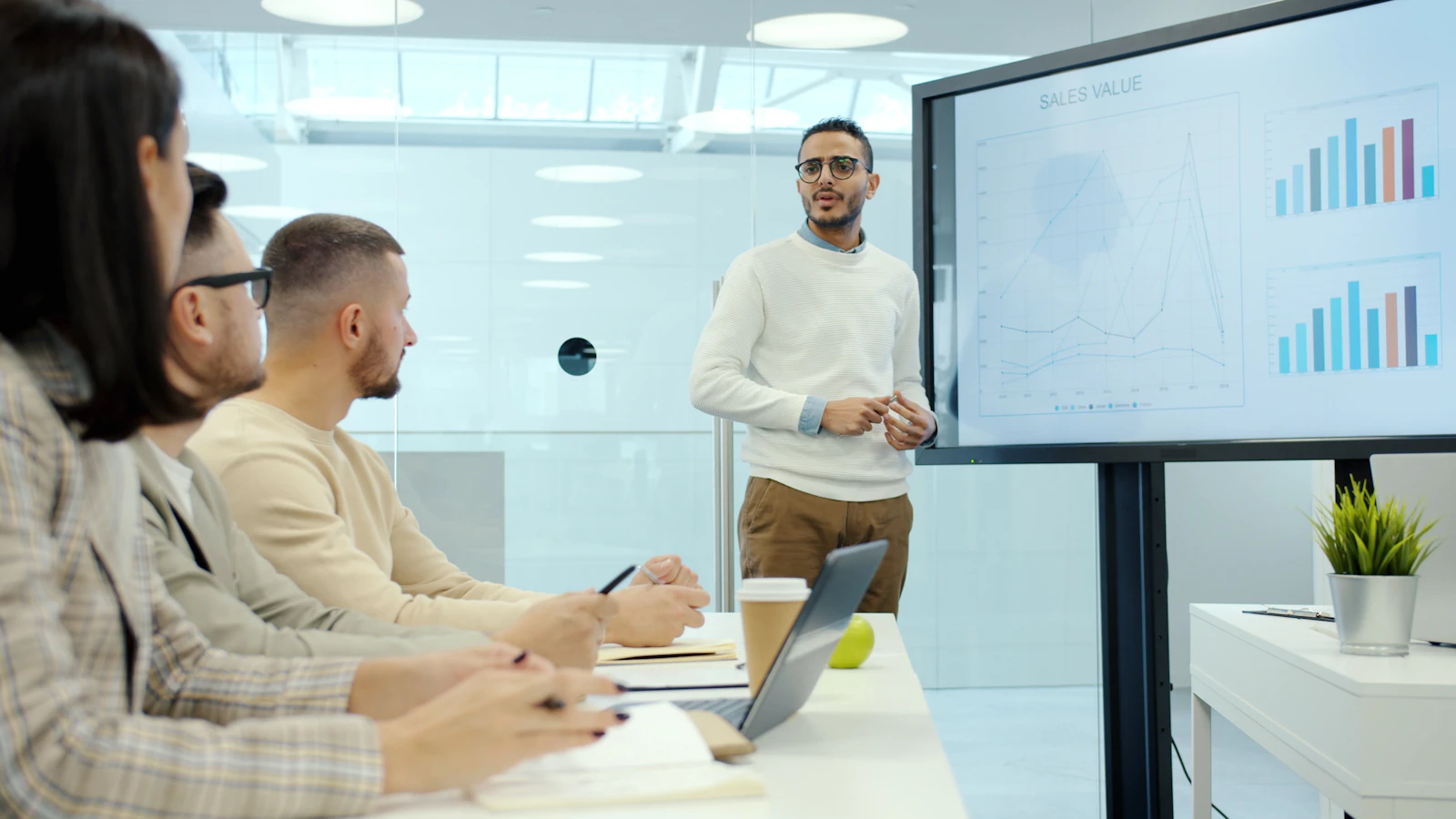 A presenter gesturing toward charts on a digital whiteboard in a meeting