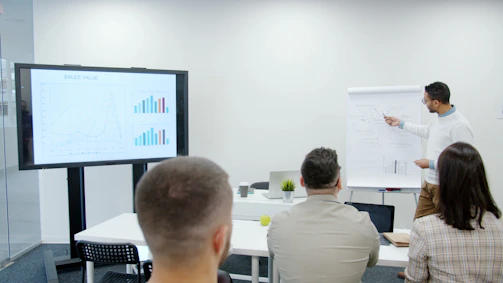 Man presents charts to seated audience in a modern office.