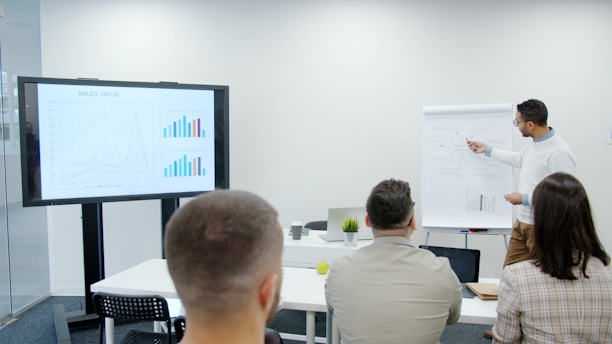 Man presents charts to seated audience in a modern office.