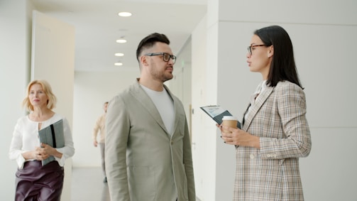 Two colleagues talking in a modern office hallway.