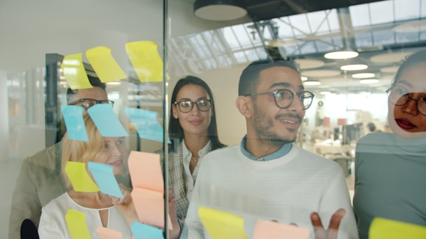 Diverse team brainstorming with sticky notes on glass.