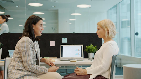 Two women talking in a modern office setting.