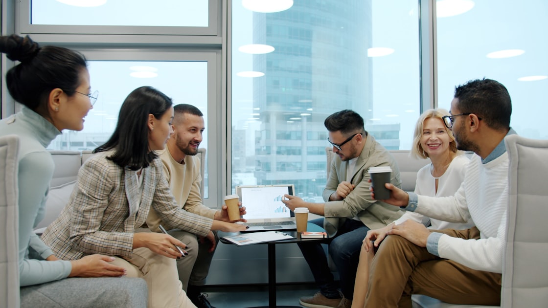 A diverse team of professionals collaborating around a laptop in a modern office meeting