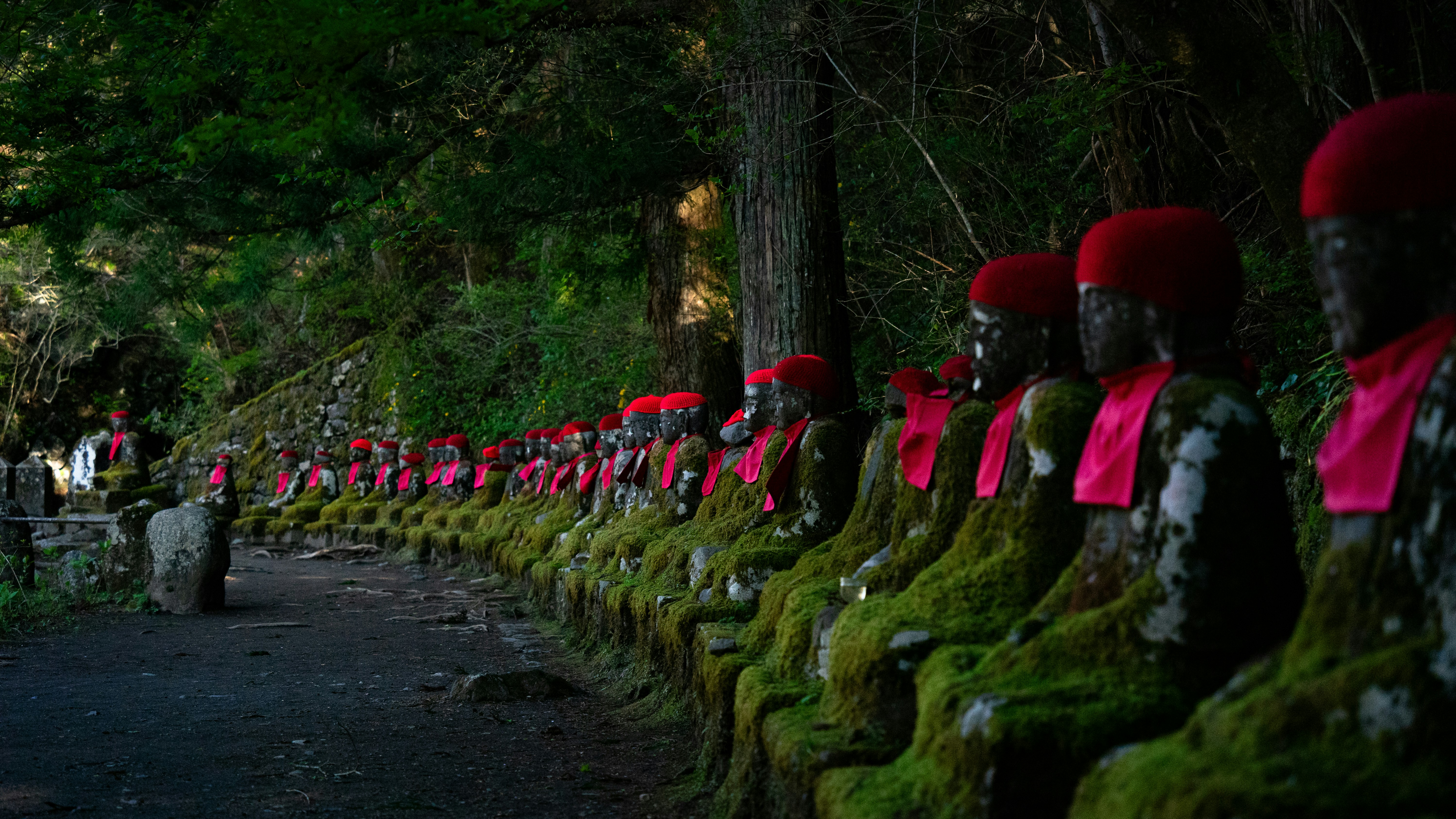 Row of moss-covered statues with red hats and sashes