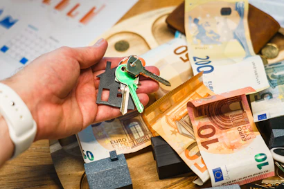 Hand holding house keys over euro banknotes and charts.