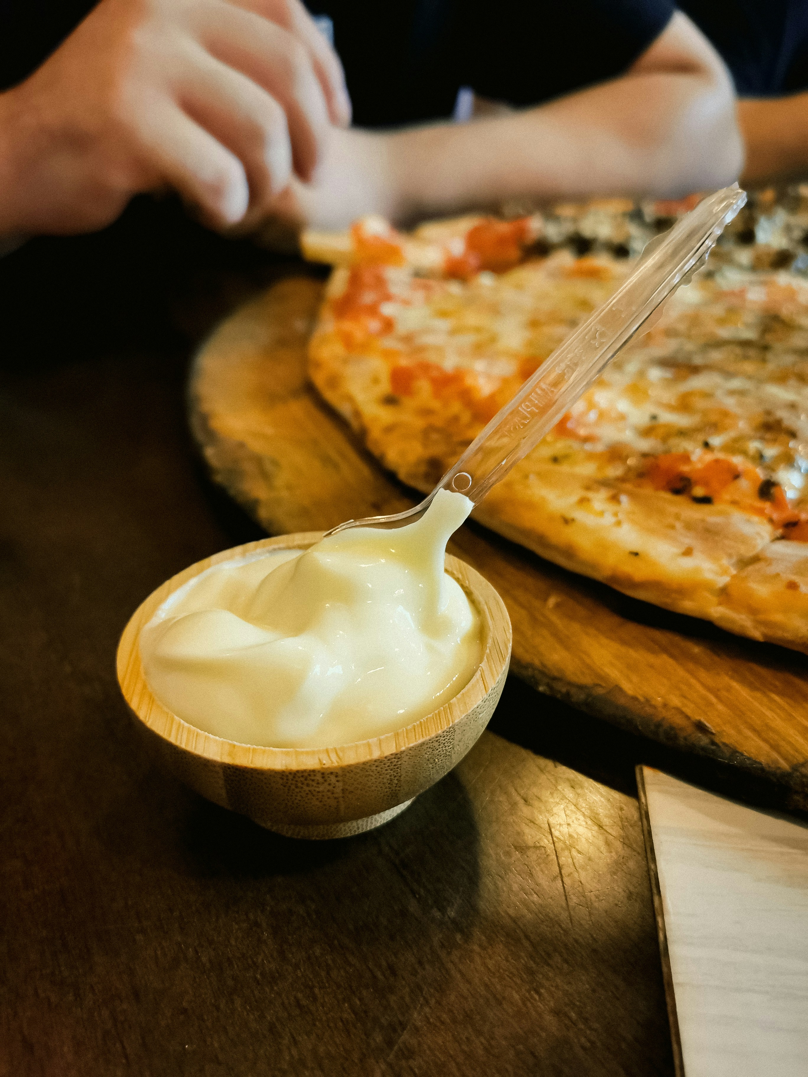 Wooden bowl of creamy sauce with pizza in background.