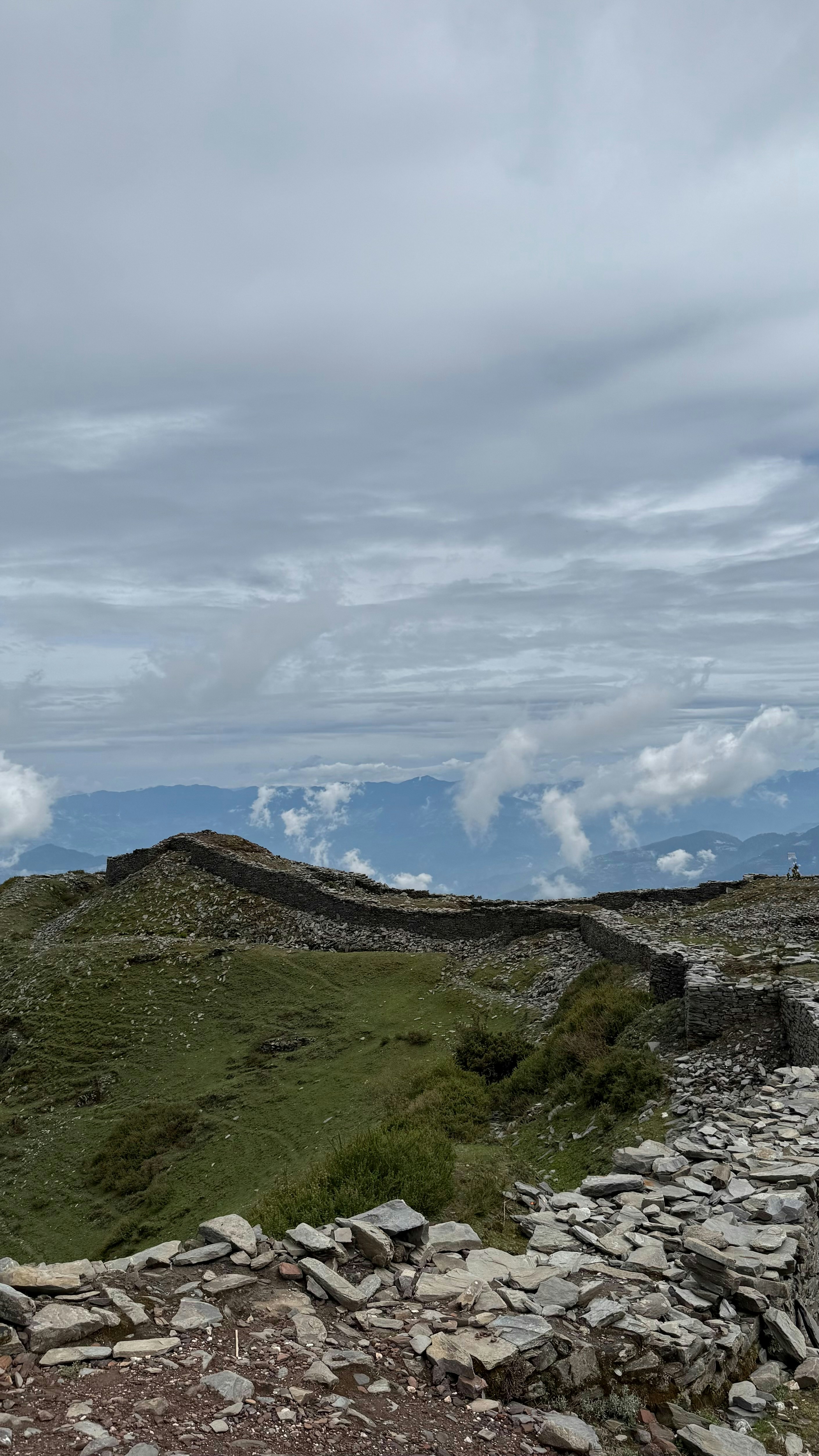 曇り空の下、草が生い茂った山の上の石造りの遺跡