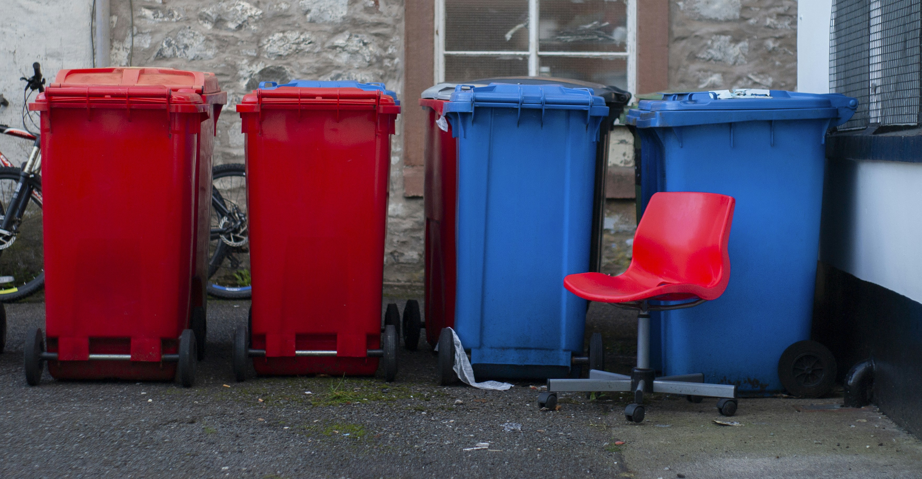 Four colorful trash bins with a red chair.