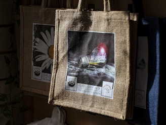 Jute bags with printed designs hanging in sunlight.