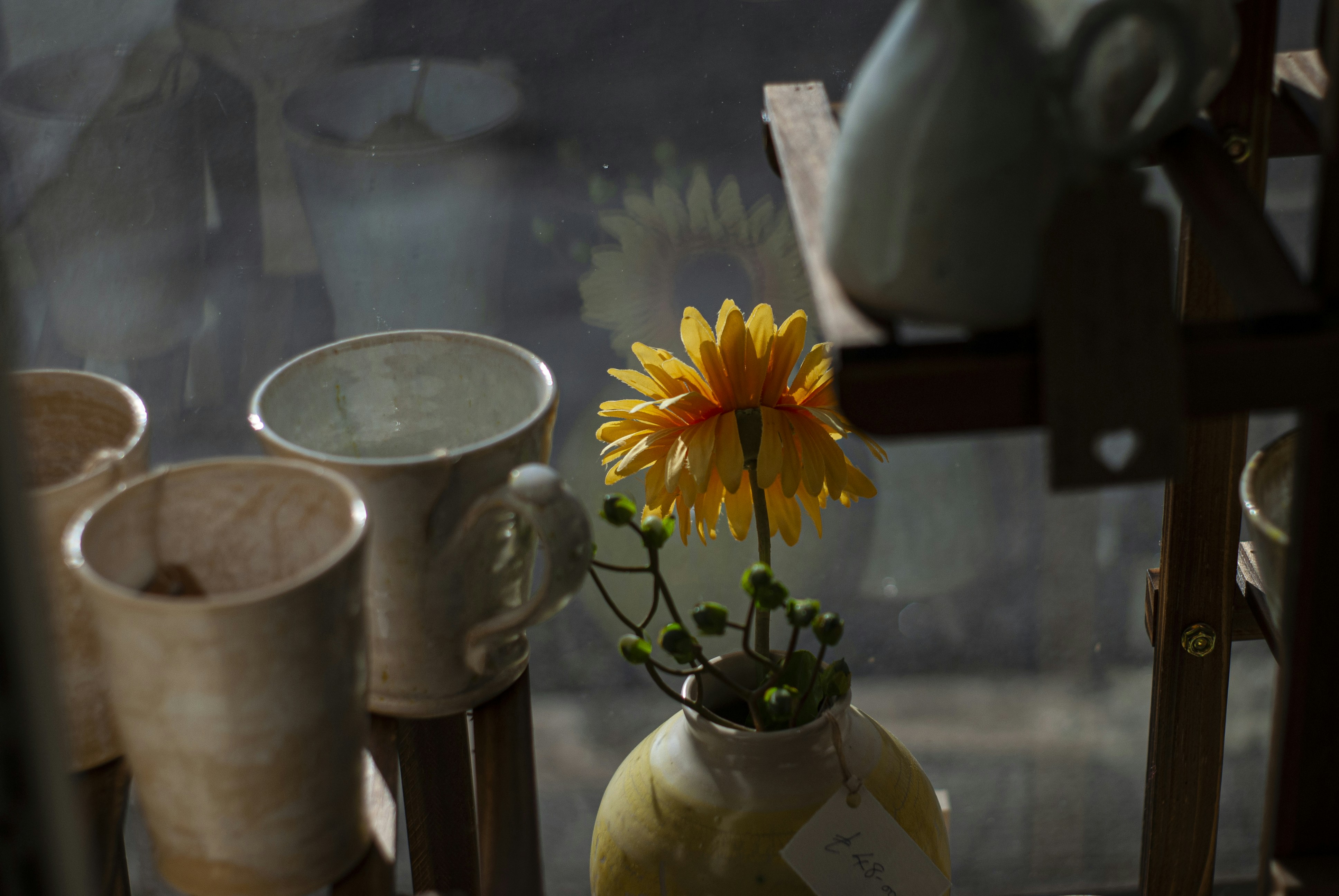 Yellow flower in vase surrounded by pottery.