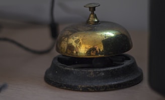 A vintage brass service bell on a wooden desk.