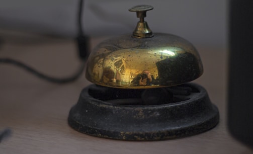 A vintage brass service bell on a wooden desk.