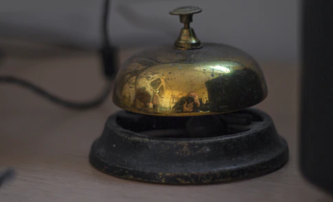 A vintage brass service bell on a wooden desk.