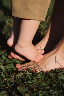 Baby's feet stepping on adult's feet in grass