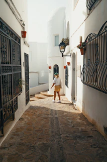 Woman walking down a narrow, sunlit mediterranean street.