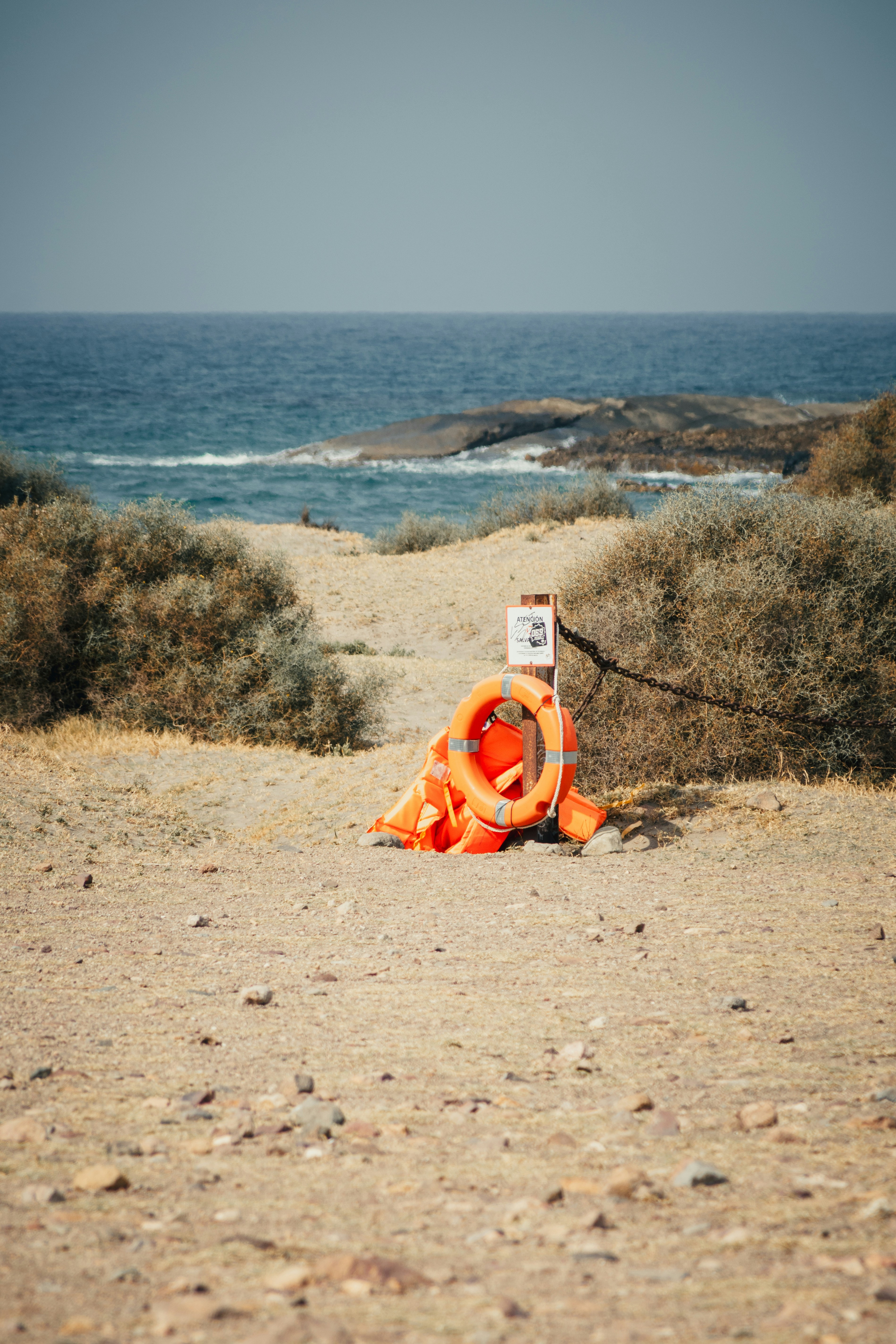 Coletes salva-vidas laranja e um sinal em uma praia arenosa.
