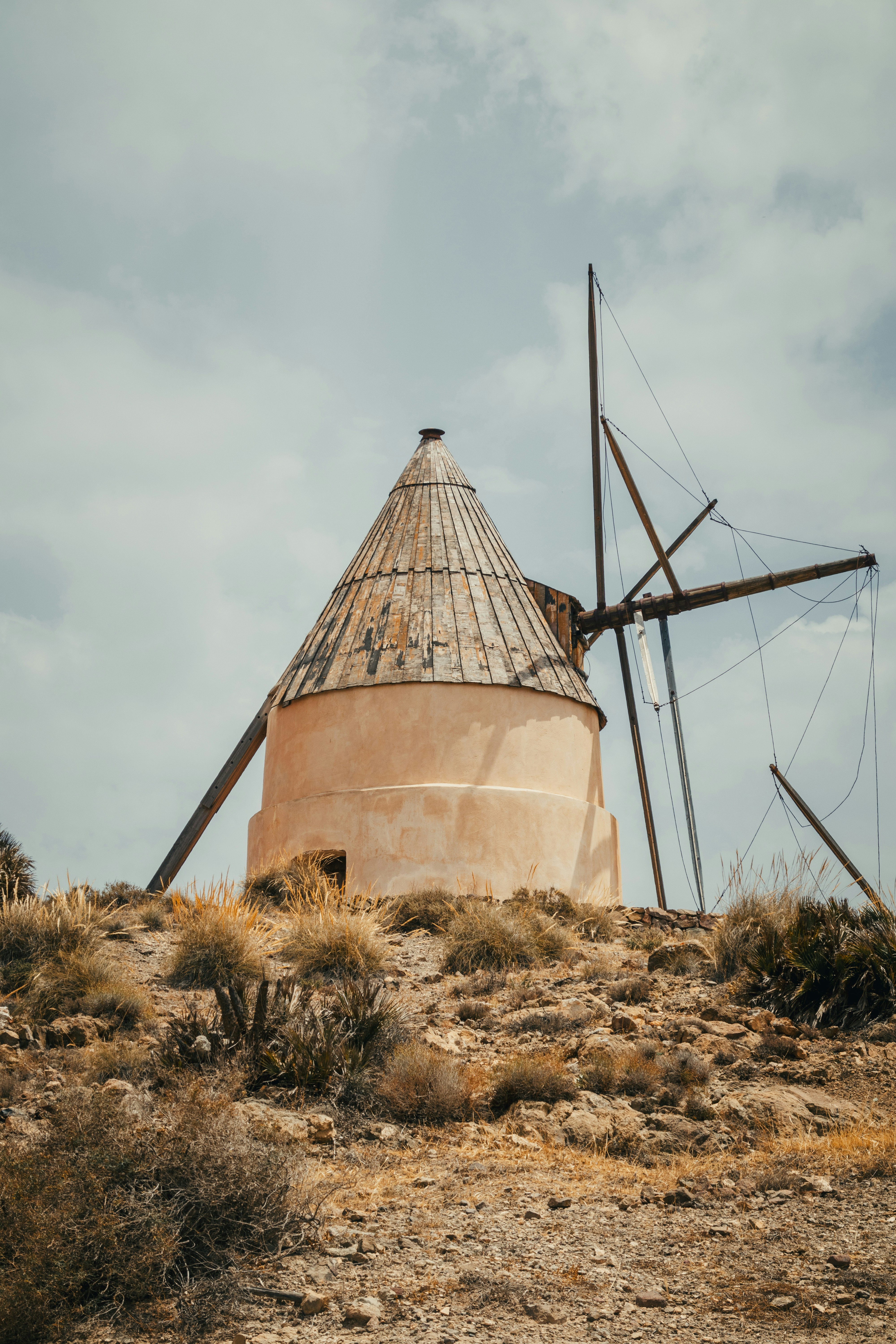 Moinho de vento velho em um monte seco, rochoso sob o céu nebuloso