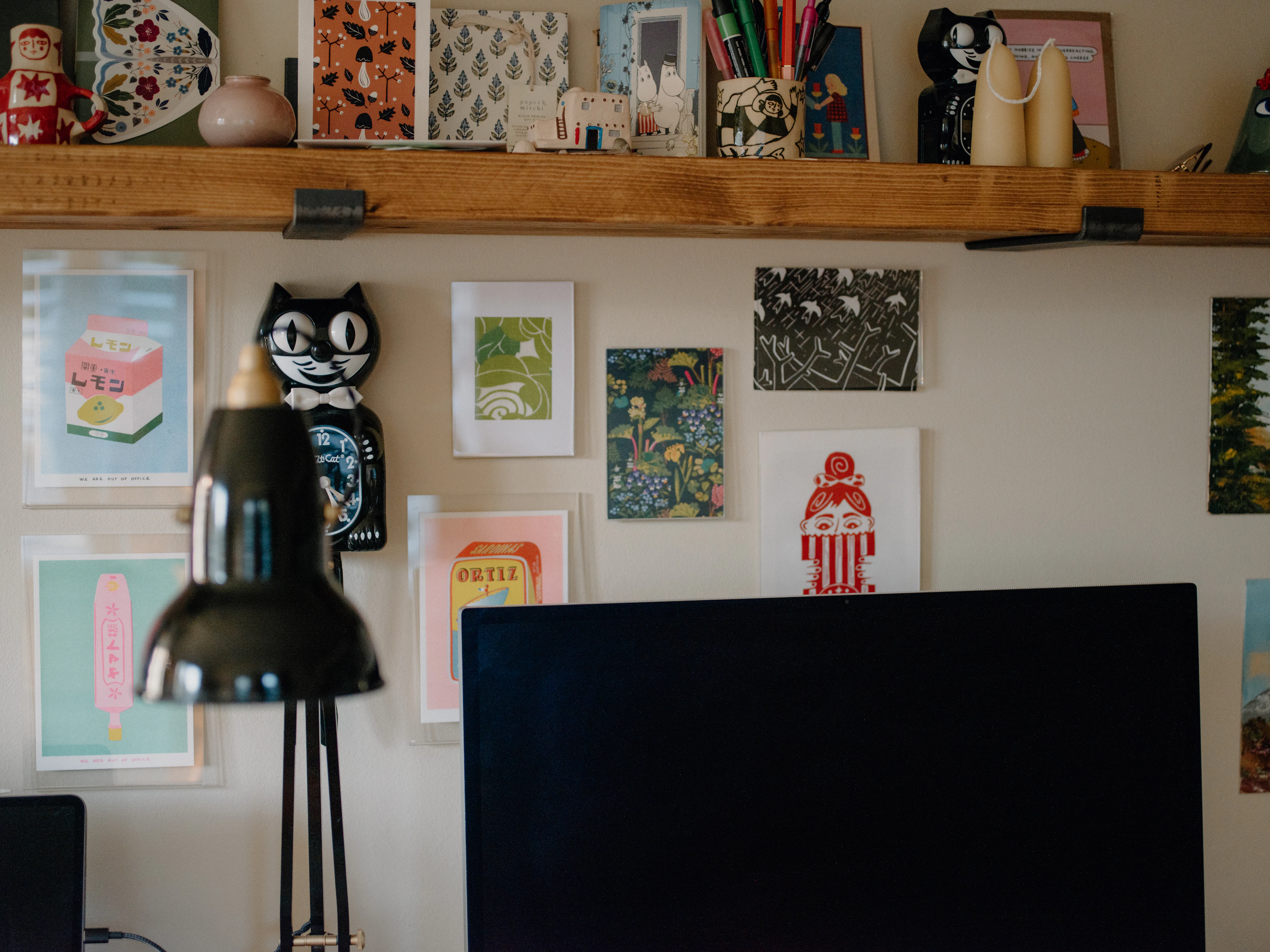 Framed prints on a wall above a desk with a black lamp.