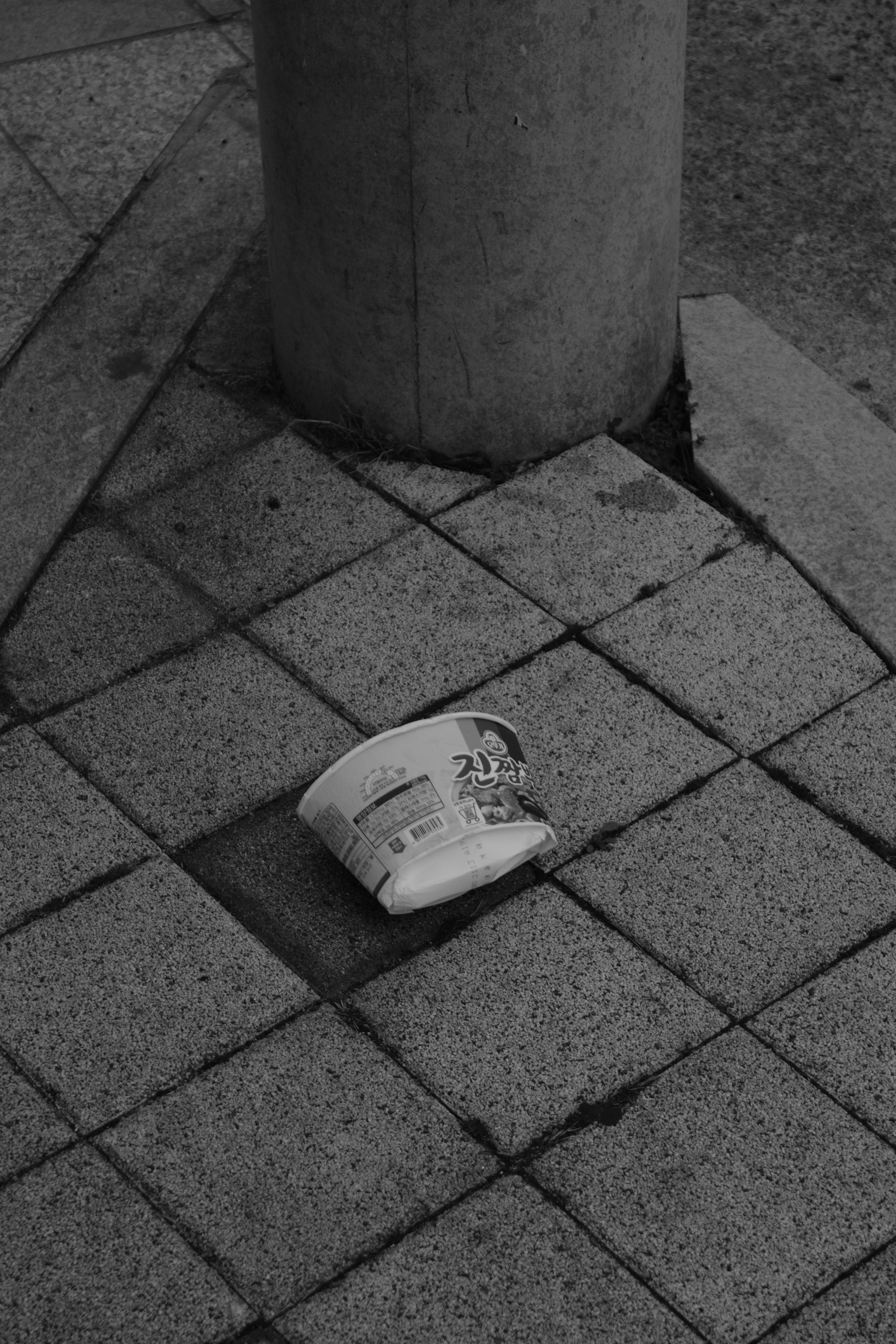 Discarded cup on a tiled sidewalk next to pole.