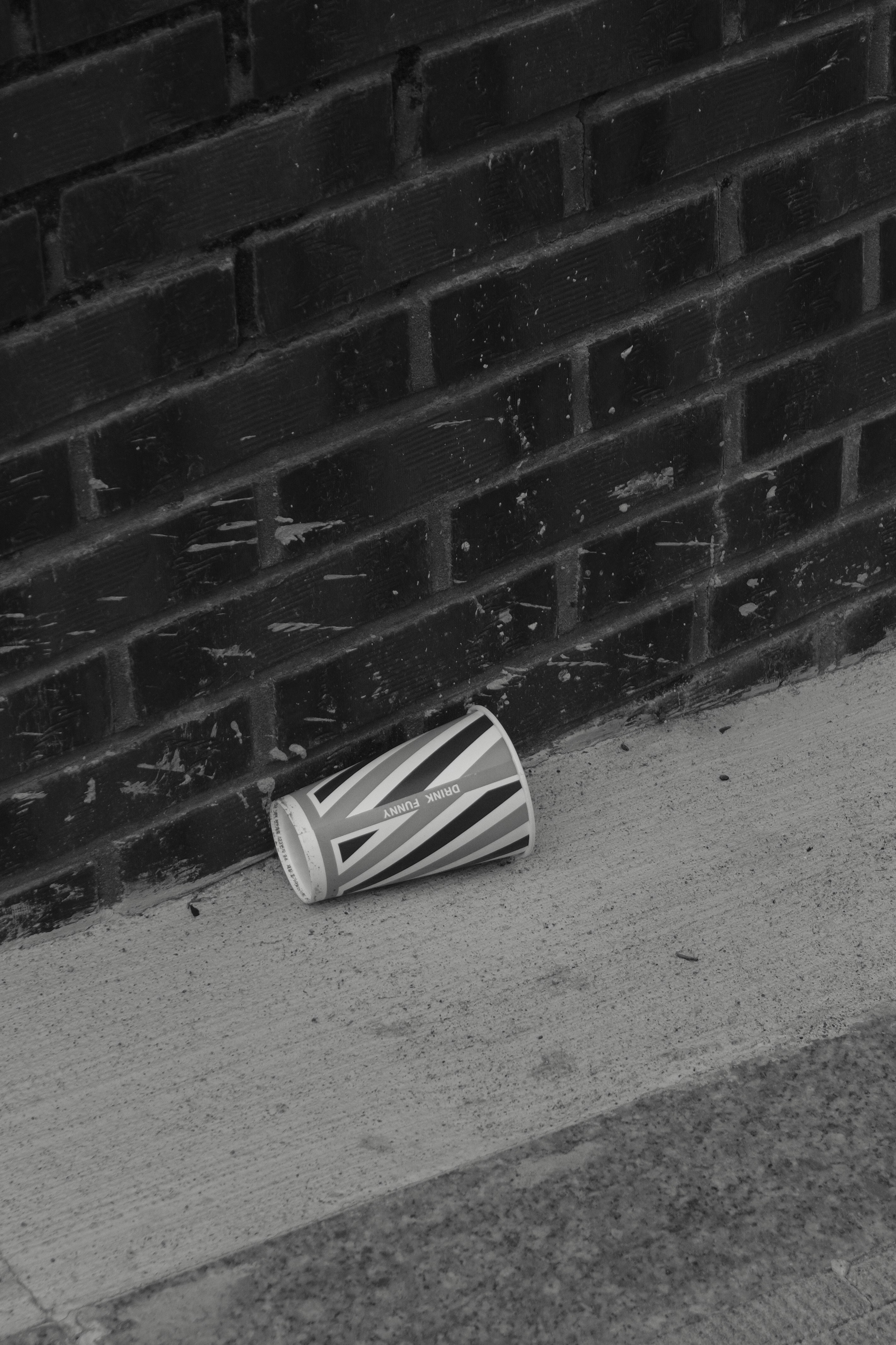 A discarded paper cup lies on a concrete sidewalk.