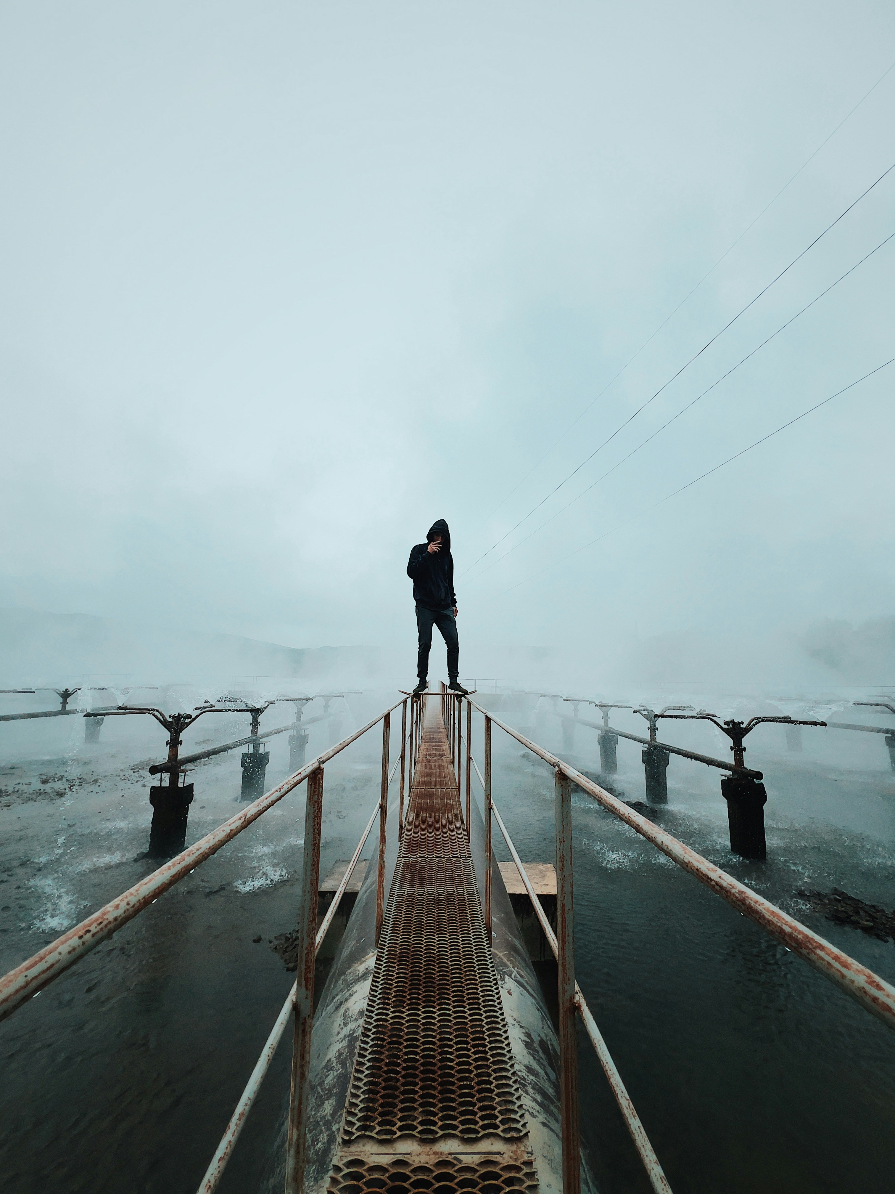 Personne debout sur une passerelle industrielle dans un paysage brumeux