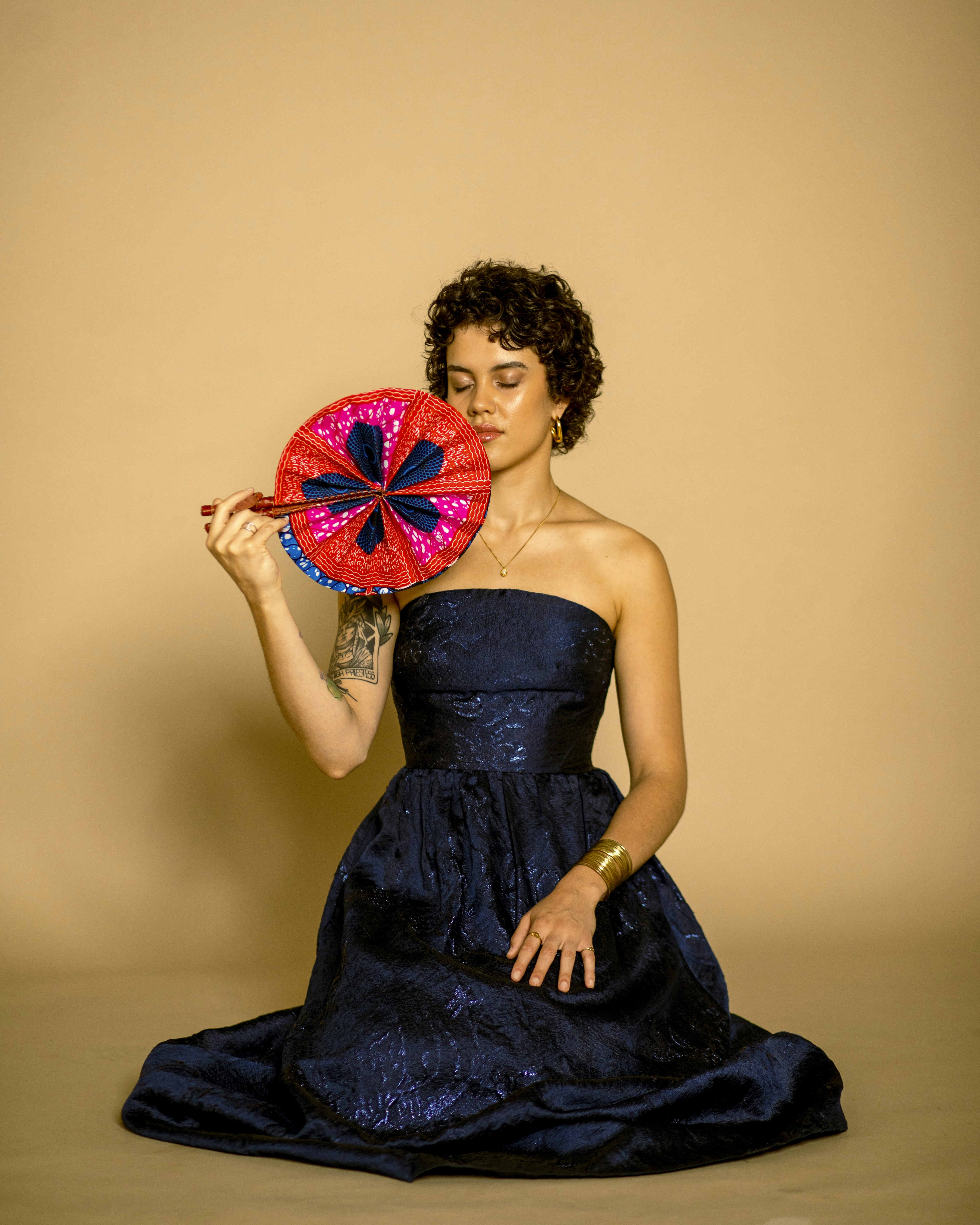 Woman in navy dress holds colorful fan.