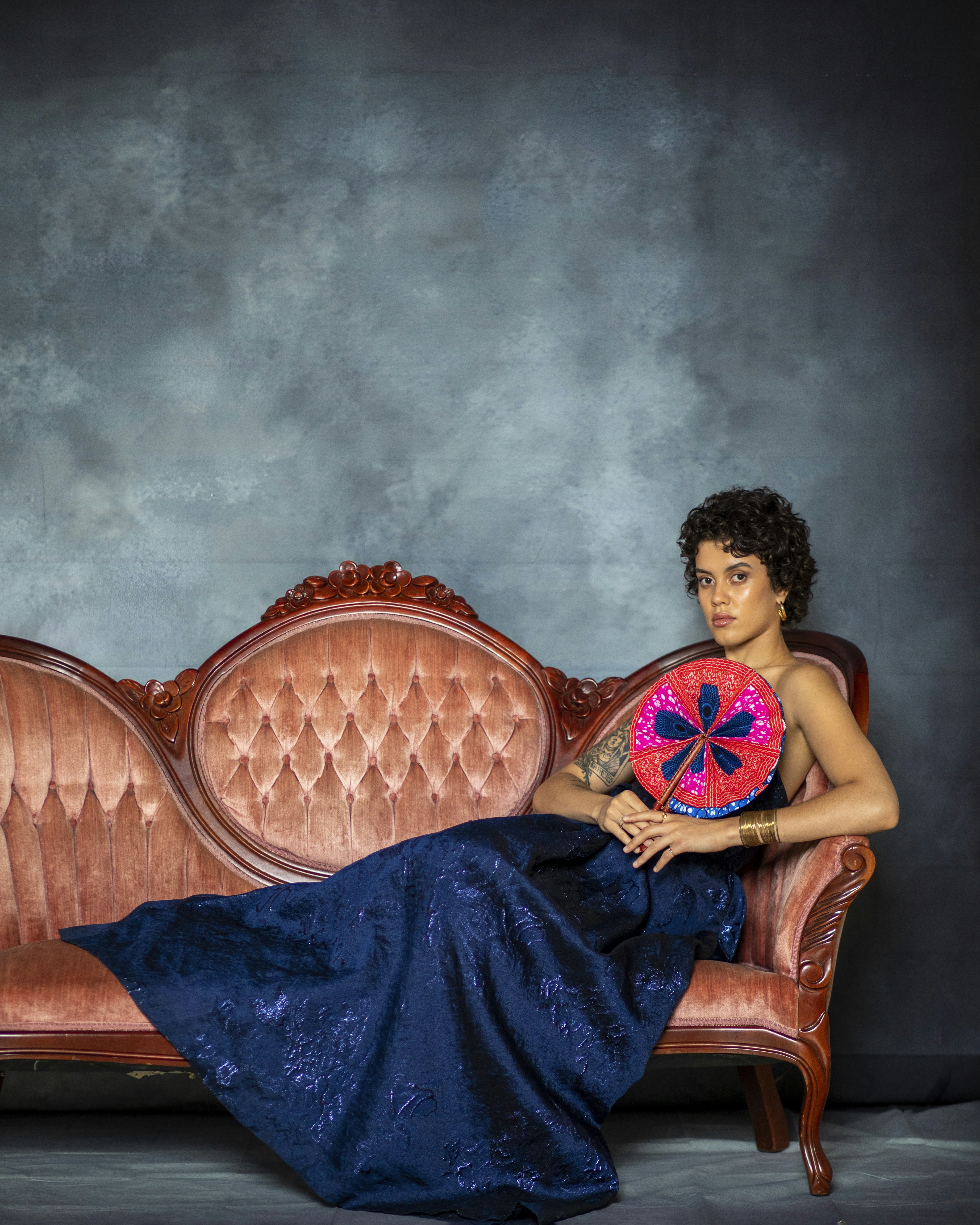 Woman in blue dress holding a fan on a sofa.