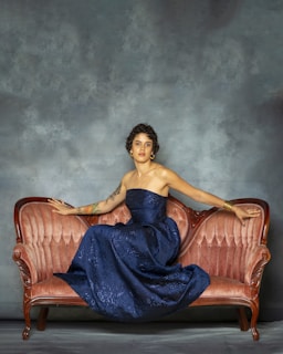 Woman in elegant blue dress sits on vintage sofa.