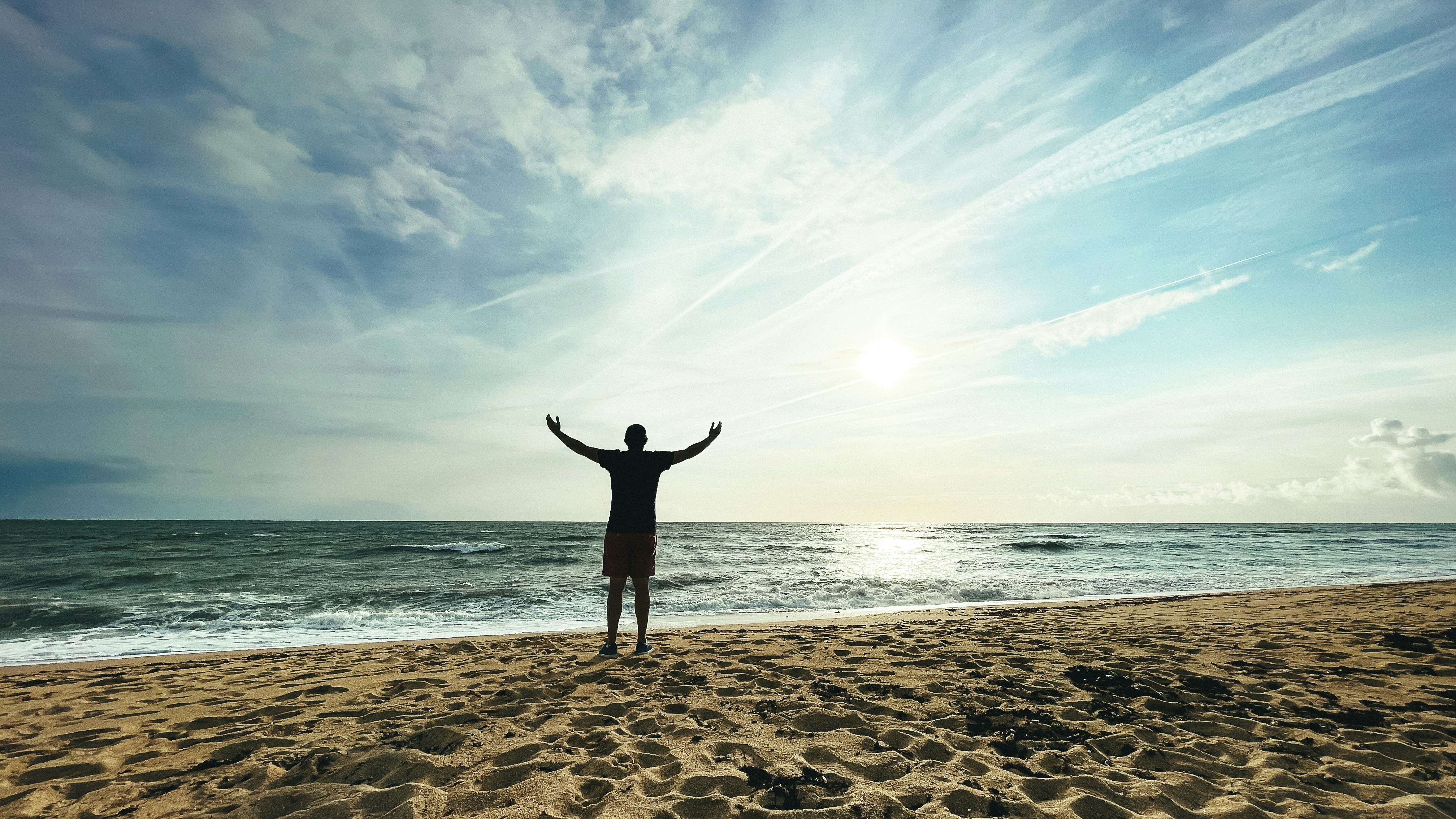 Person with arms raised on beach at sunset