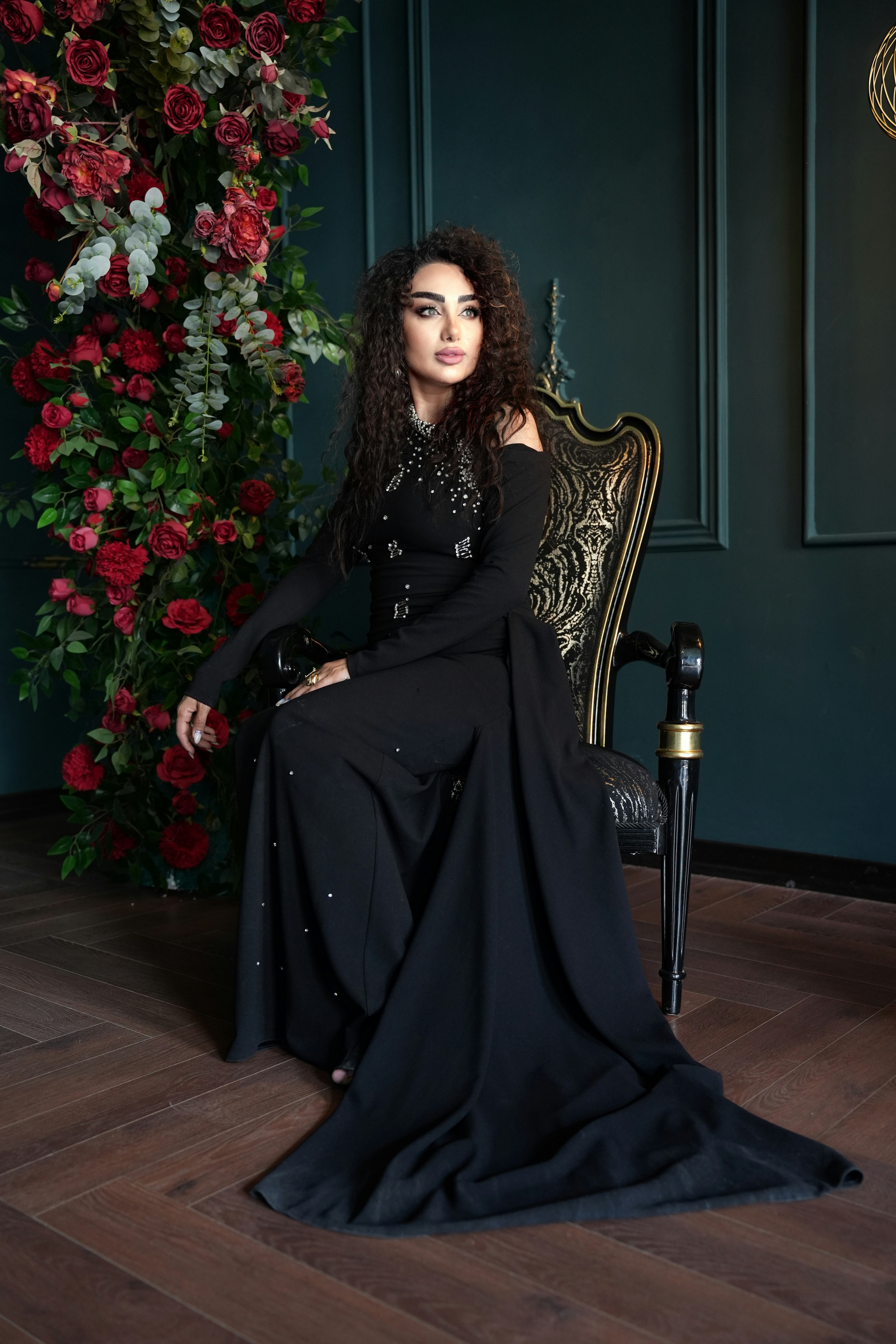 Woman in black dress sits on ornate chair near roses.