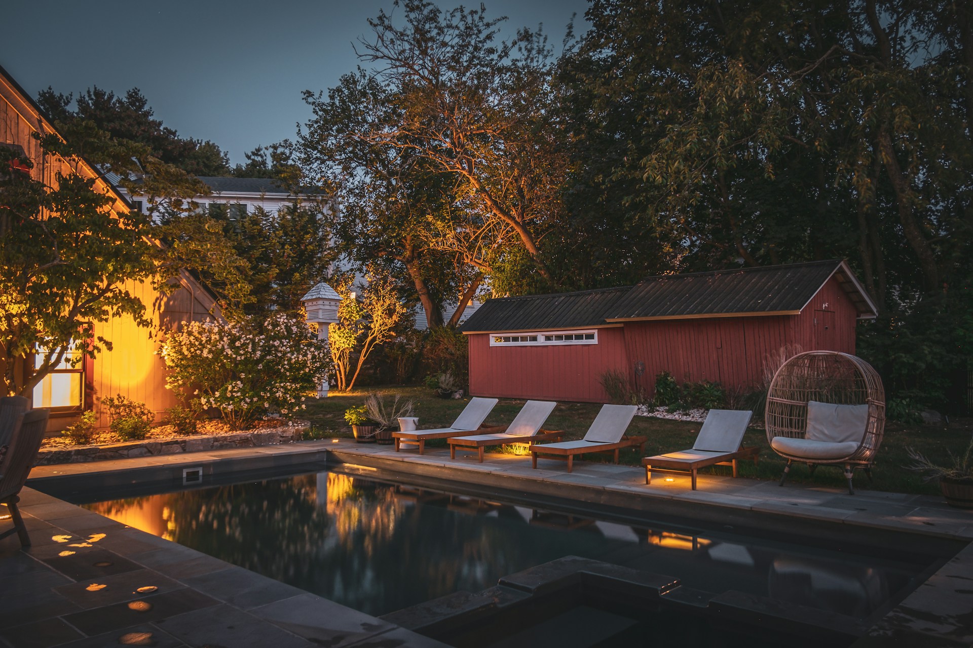 Poolside lounge chairs next to a red building at dusk.